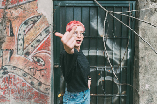 young woman pink hair outdoor showing middle finger - aggression, hand gesture, rudeness concept
