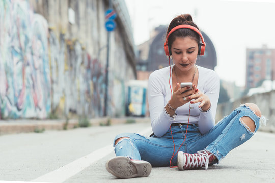 young woman outdoors listening music with headphones using smart phone - relaxing, enjoying, technology concept