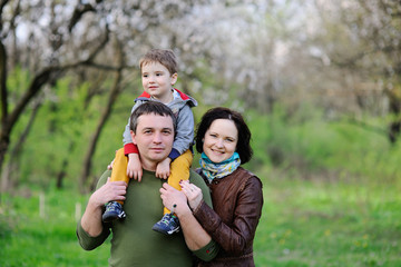 Fototapeta premium Young family - mom, dad and little son playing in the park against the background of spring green trees