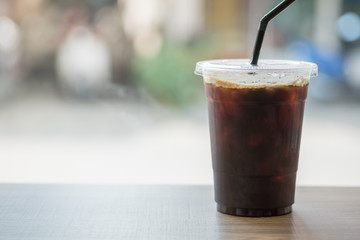 Close up of take away plastic cup of iced black coffee (Americano) on wooden table.