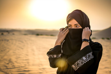 Portrait of a young Arab woman wearing traditional black clothing in the desert during sunset.