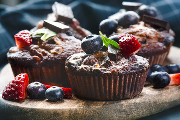 Fresh, blueberry muffins with strawberry, chocolate on a wooden board and stone background with sugar and fruits. Food background. Concept of pastry. 