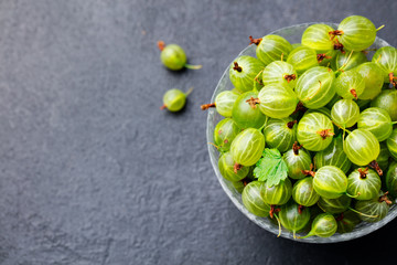 Gooseberries in glass bowl on black stone slate background. Top view. Copy space.