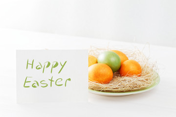 Happy Easter concept. Easter eggs in nest on white wooden table and a white card with the inscription Happy Easter. Angle view.