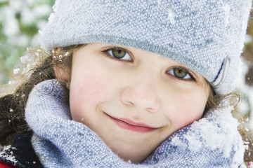 In winter, in the forest, there is a beautiful little girl in a hat and scarf. Close-up.