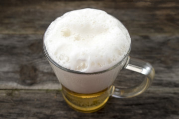 Mug with a frothy beer close-up on a wooden background.