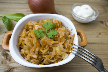 Appetizing stewed cabbage close-up, and onion, sour cream and lettuce leaves in the background.