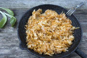 Appetizing fried cabbage in an old frying pan on an old wooden background close-up.