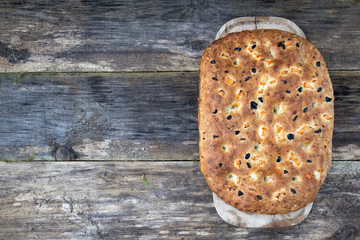Traditional Italian focaccia homemade bread with tomatoes and olives, on a wooden background and copy space.