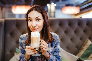 Beautiful young brunette eastern woman sitting in cafe and drinking latte coffee