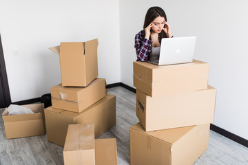 Young woman moving in a new flat, sitting on the floor and surfing the web on a laptop in search of new decorating ideas.