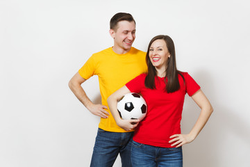 Fun smiling cheerful young couple, woman, man, football fans in yellow and red uniform cheer up support team holding soccer ball isolated on white background. Sport, family leisure, lifestyle concept.