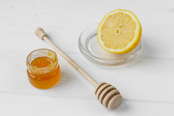 Glass jar of honey on a textile tablecloth. Glass saucer and wooden spoon, kitchen utilities. Home made organic mask ingredients. Healthy eco lifestyle. Food blog illustrations. Honey and lemon
