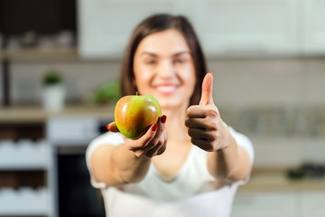 Woman in white t-shirt holding green apple in the kitchen
