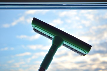 Green mop cleaning clear glass of window and blue sky with cloud background