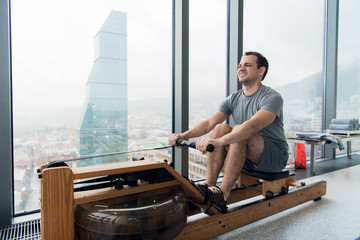 Man working out on row machine in fitness studio at scyscraper luxury hotel gym