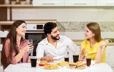 Cute young guys having friendly and joyful talk while having fast food meal, indoor shot in cozy white kitchen