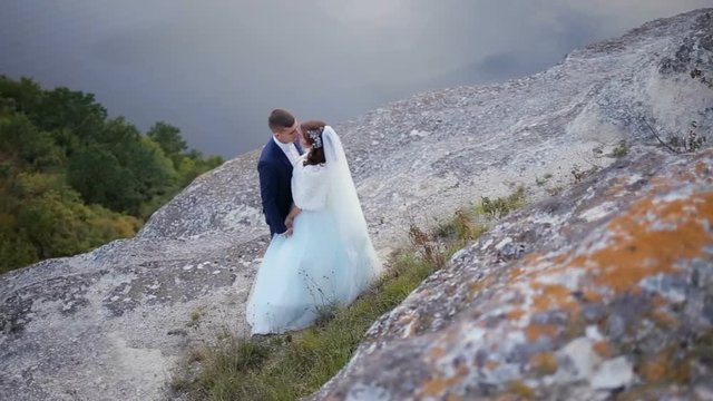 Wedding couple tenderly kissing on the mountain peak edge with amazing view