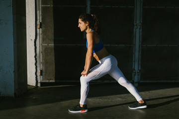 Fit female athlete stretching legs for warming up before urban running workout. Fitness young woman exercising outside.