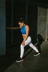 Fit female athlete stretching legs for warming up before urban running workout. Fitness young woman exercising outside.