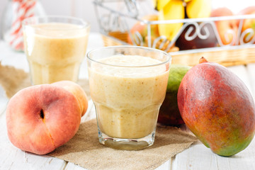Mango and peach smoothie on wooden table with ingredients.