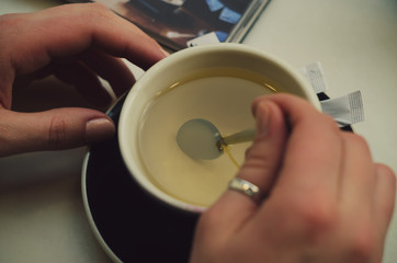 Fototapeta na wymiar hand hold cup with green tea with teaspoon and magazine close up photo