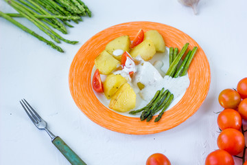 Potatoes and asparagus with tomatoes and tartar sauce on plate ready to eat.