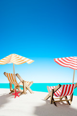 Two sun loungers under an umbrella on the sandy beach by the sea and the sky with copy space