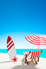 Deck chair under an umbrella with a surfboard on sandy beach by the sea and sky with copy space