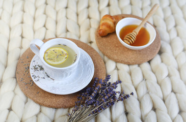 Cup with lavender tea, citrus and honey, croissant, white pastel giant knit blanket, bedroom, flowers tulips, spring, woman day, morning concept