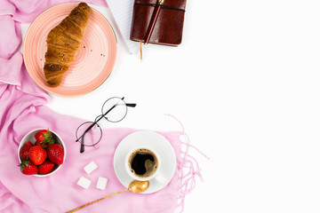 Beautiful flatlay arrangement with wholewheat croissant, cup of espresso coffee, fresh strawberries and business accessories: concept of busy morning breakfast, white background. Copyspace