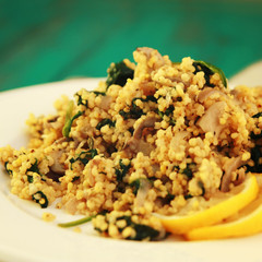 Millet with mushrooms and spinach. Vegan dish. Vegetarian couscous on the round white plate. Close up. Toned photo.