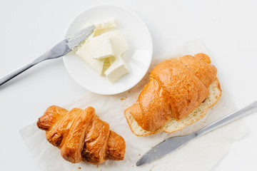two croissants and butter on a white table, top view.