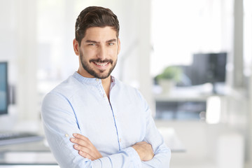 Confident young businessman portrait. Portrait of a casual young man standing at office, looking at camera and smiling. 