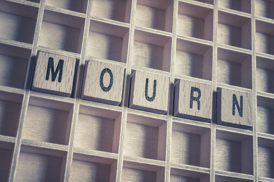 Closeup Of The Word Mourn Formed By Wooden Blocks On A Wooden Floor