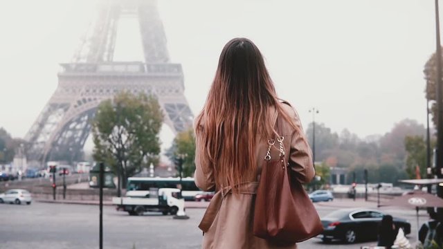 Young stylish woman taking photo of Eiffel tower in fog on smartphone. Girl traveling in Paris, France alone.
