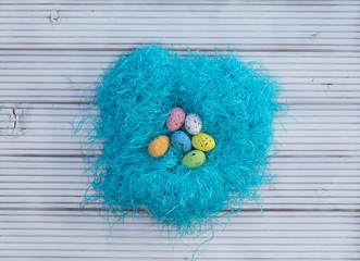 Fototapeta na wymiar colored Easter eggs in a nest on a white wooden background