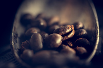 Grains of coffee lie in an old antique spoon. Unusual photo low key.