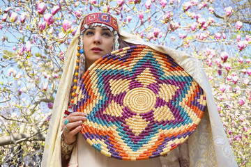 Girl against of magnolia flowers in national Palestinian costume, with head covered. 