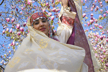 Girl against of magnolia flowers in national Palestinian costume, with head covered. 
