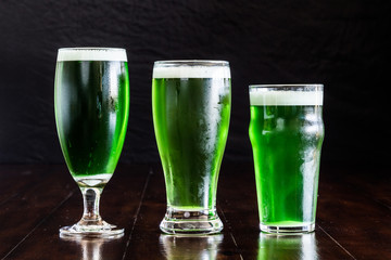 3 beer glasses, Belgian ale, classic pilsner and English pub with green beer on rustic wood table.