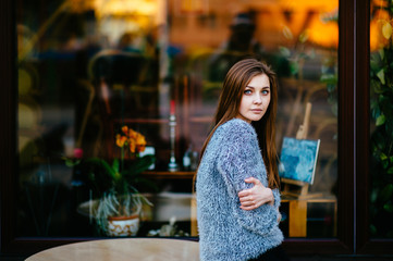Young odd beautiful model girl with sensual pensive face posing for camera outdoor in front of shop showcase with abstract reflections in morning. Amazing teenager female with blue eyes mood portrait.