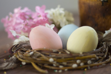 three raw colored eggs blue pink yellow in the nest on wooden background flowers cake Easter spring Christian holiday Holy