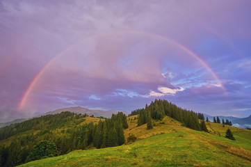Fototapeta na wymiar Mountain nature photo background with bright rainbow in dramatic cloudy sky