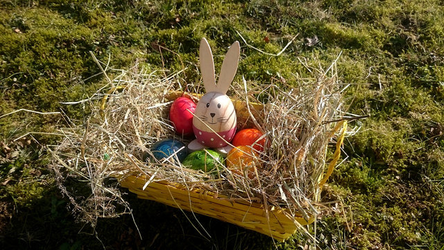 Osterkorb mit bunten Eiern und Deko-Häschen auf der Mooswiese