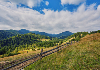 Fototapeta na wymiar composite landscape. fence near the cross road on hillside meadow in mountains.