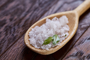 Crystal sea salt in a wooden spoon over vintage wooden background, top view, close-up, selective focus