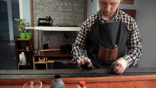 In the workshop, a specialist colors the belt in black. Procedure for the manufacture of leather belts