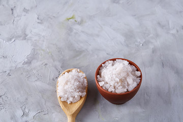 Crystal sea salt in a wooden spoon over light background, top view, close-up, selective focus