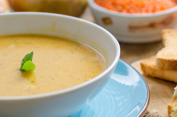 the lentil soup in the white plate is on the table. There are lentils, carrots, bread, onions on the table.